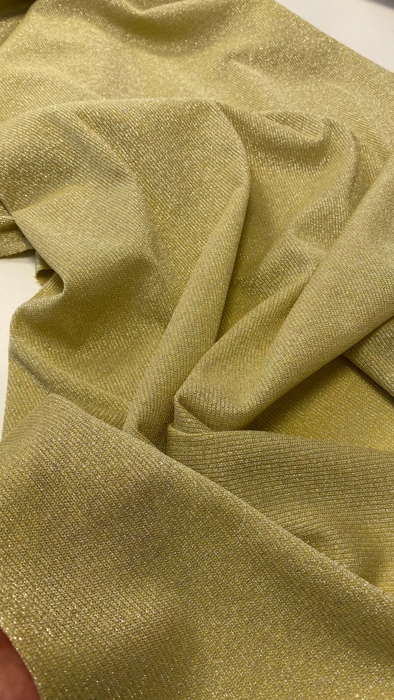 May include: A close-up of a gold fabric with a subtle shimmer. The fabric has a ribbed texture and is folded in a way that shows the texture and shimmer.