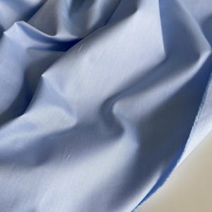May include: A light blue fabric with a smooth, slightly textured surface. The fabric is folded and draped, showing its soft and flowing nature.
