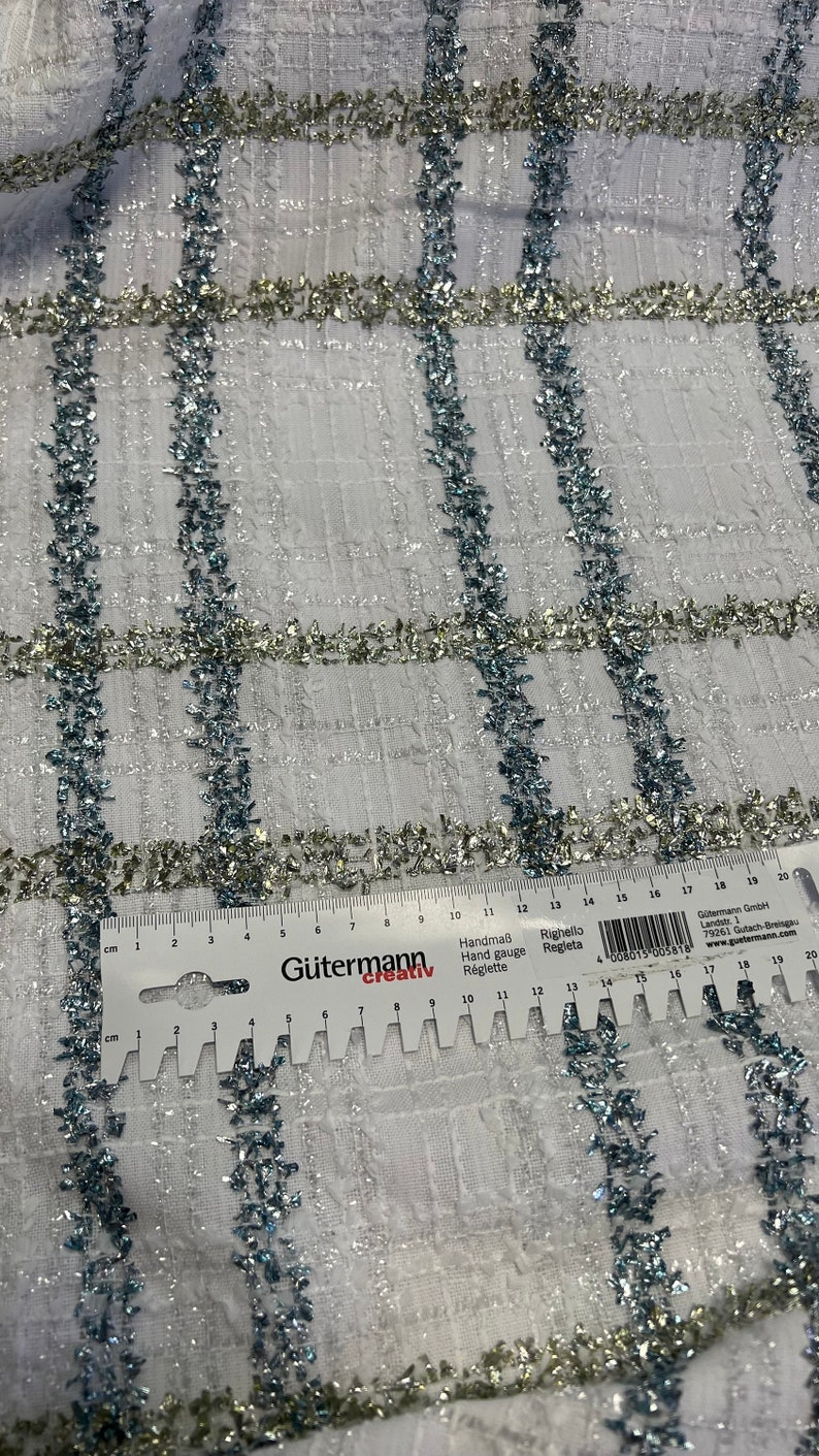 May include: White fabric with a grid pattern, accented with silver and blue glitter. The fabric is measured with a ruler in inches.