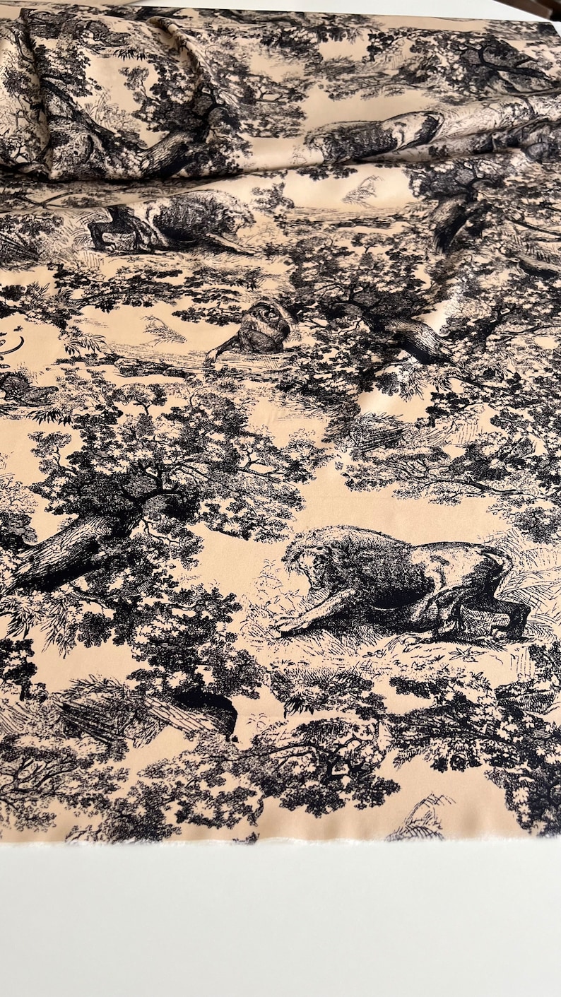 May include: Black and white fabric with a repeating pattern of trees, leaves, and animals. The fabric has a beige background.