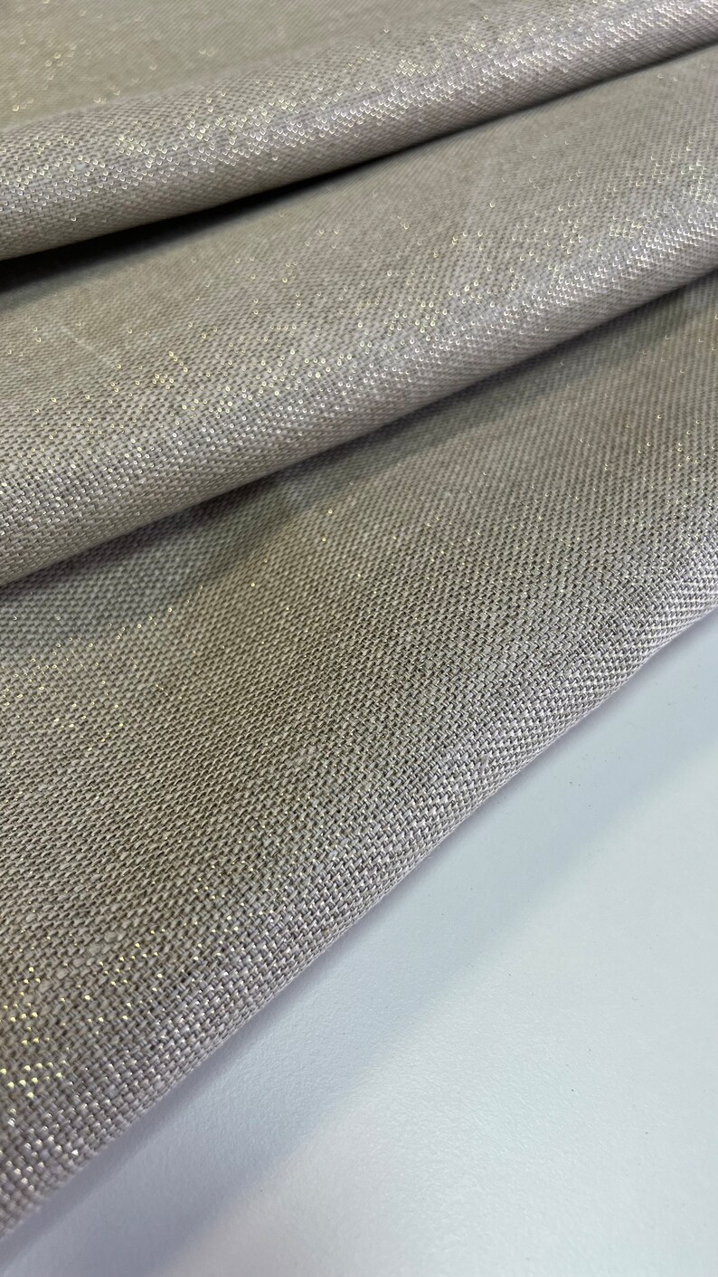 May include: Close-up of a beige fabric with a subtle shimmer. The fabric has a woven texture and a slightly rough surface.