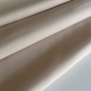 Peut inclure: Gros plan sur un tissu beige plié. Le tissu a une texture subtile et semble être un matériau de poids moyen. Les plis créent des ombres et des reflets, ajoutant de la profondeur à l'image. La couleur est une teinte neutre, adaptée à diverses applications.