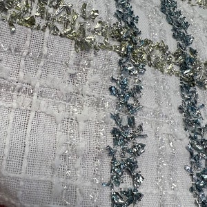 May include: White fabric with a woven texture and silver and blue embellishments. The fabric has a subtle checkered pattern.