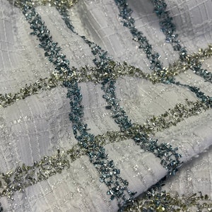 May include: White fabric with a checkered pattern. The fabric is embellished with silver and blue glitter thread.