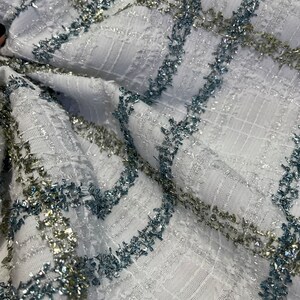 May include: White fabric with a textured weave and silver and blue glitter stripes. The fabric is folded and the glitter stripes are visible.