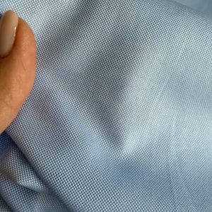 May include: Close-up of a light blue fabric with a textured weave. The fabric is smooth and has a subtle sheen.