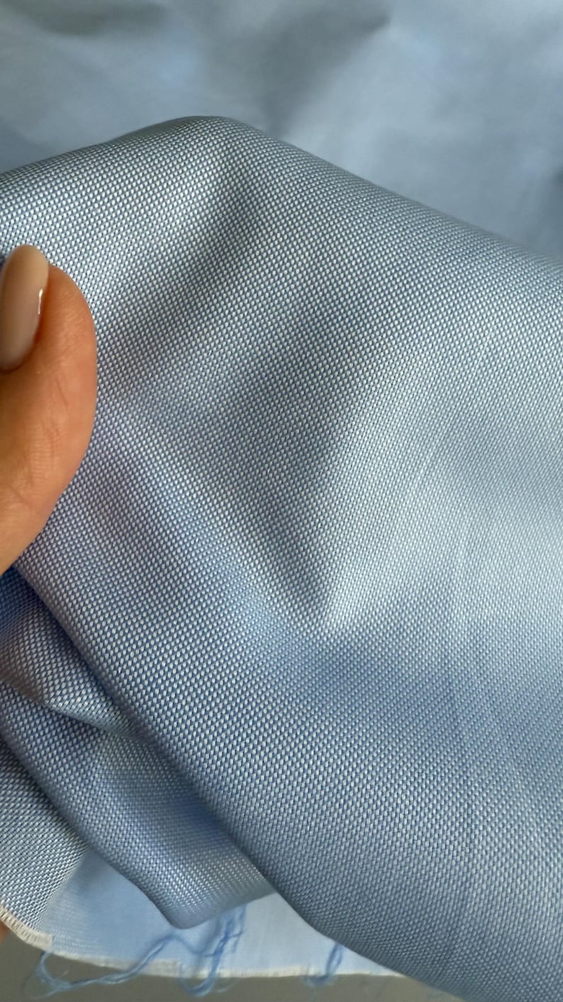 May include: Close-up of a light blue fabric with a textured weave. The fabric is smooth and has a subtle sheen.