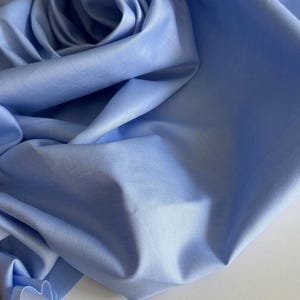 May include: A close-up of a light blue fabric with a smooth, textured surface. The fabric is folded and draped, creating a soft, flowing look.