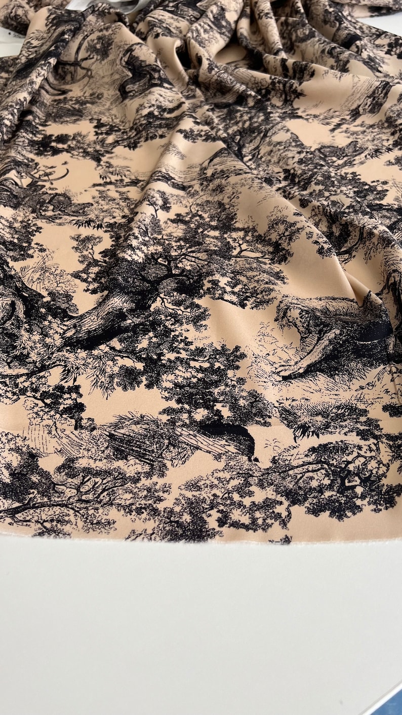 May include: Beige fabric with a black and white toile pattern featuring trees and foliage.