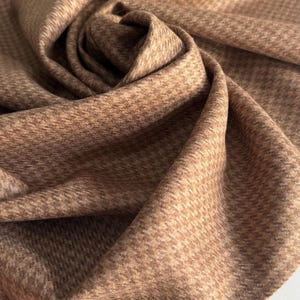 May include: Close-up of a folded fabric with a houndstooth pattern in shades of brown and tan. The fabric is soft and textured, with a subtle sheen. The pattern is small and evenly spaced, creating a classic and elegant look. Ideal for apparel and home decor.