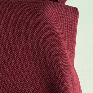 Pu&ograve; includere: Primo piano di un tessuto color borgogna con un motivo a nido d'ape testurizzato.