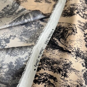 May include: Close-up of a beige fabric with a black and white toile pattern. The fabric has a white label that reads "Made in Italy 95% Cotton 5% Elastane".
