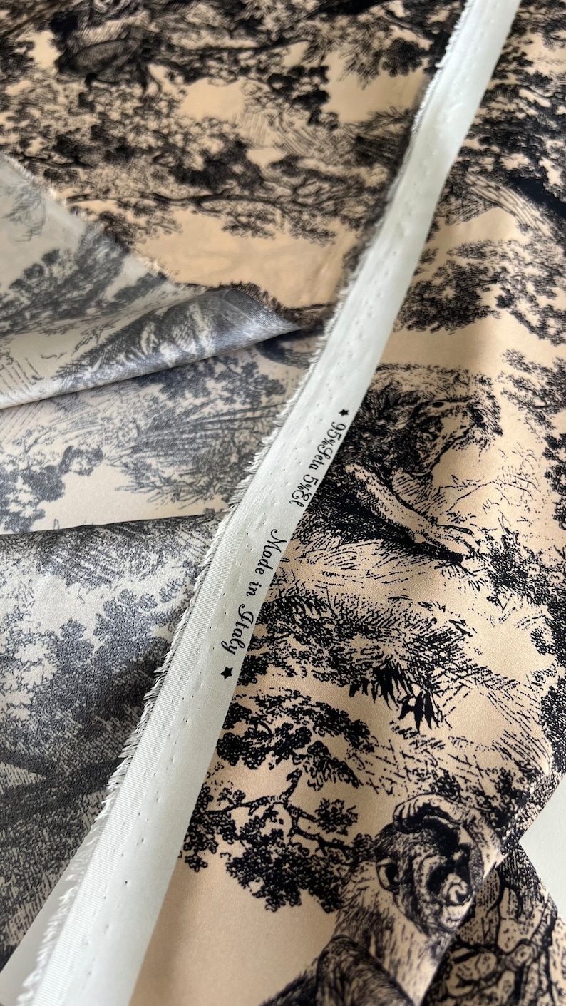 May include: Close-up of a beige fabric with a black and white toile pattern. The fabric has a white label that reads "Made in Italy 95% Cotton 5% Elastane".