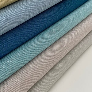 May include: A stack of six rolls of sparkly fabric in various shades of blue, green, and beige. The fabric has a ribbed texture.