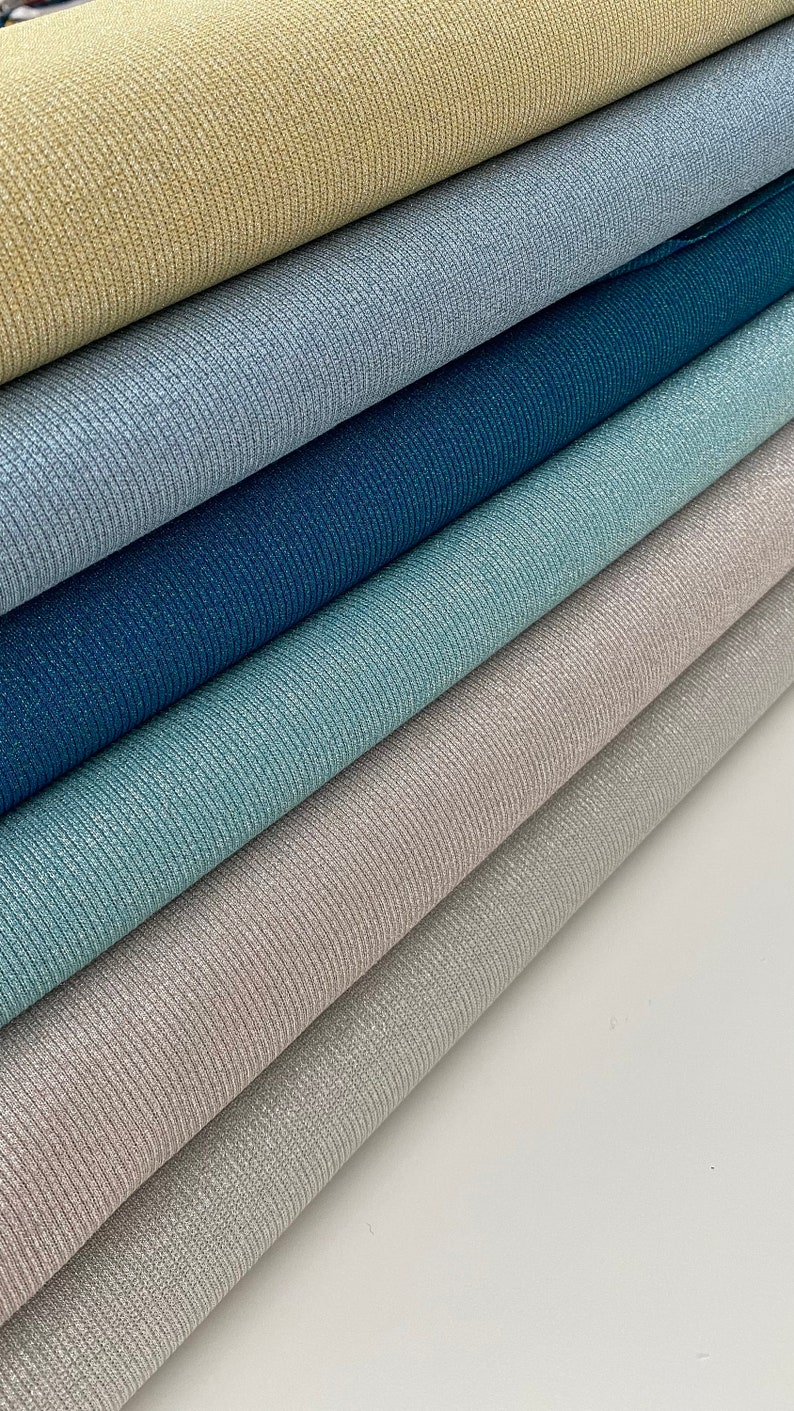 May include: A stack of six rolls of sparkly fabric in various shades of blue, green, and beige. The fabric has a ribbed texture.