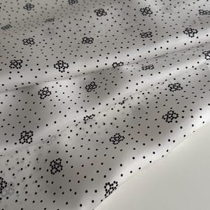 May include: White fabric with a black polka dot and floral pattern. The fabric is folded in half and the pattern is visible on both sides.
