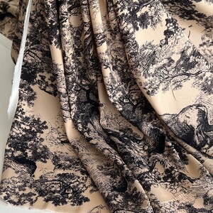 May include: Beige fabric with a black and white print of trees and foliage. The fabric is folded and draped on a white surface.