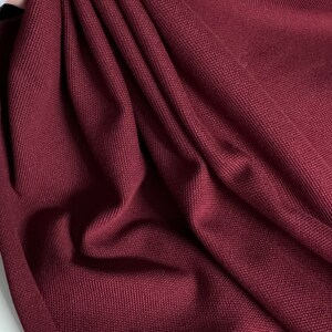 Pu&ograve; includere: Primo piano di un tessuto color borgogna con trama testurizzata. Il tessuto &egrave; piegato e drappeggiato, mostrando la sua texture morbida e flessibile.