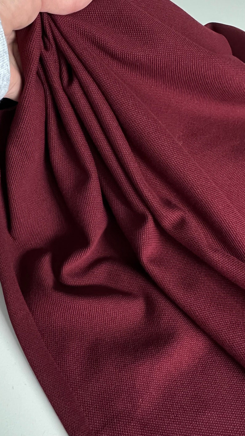 Pu&ograve; includere: Primo piano di un tessuto color borgogna con trama testurizzata. Il tessuto &egrave; piegato e drappeggiato, mostrando la sua texture morbida e flessibile.