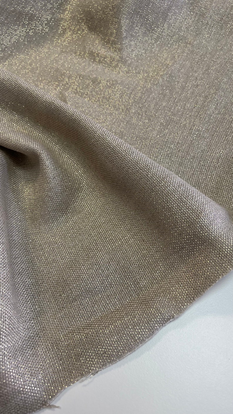 May include: A close-up of a beige fabric with a subtle shimmer. The fabric has a woven texture and a subtle sheen.