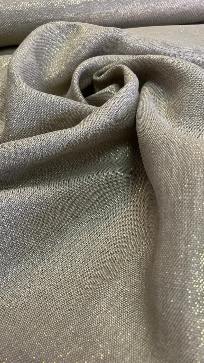 May include: Close-up of a silver fabric with a subtle shimmer. The fabric has a woven texture and a soft, drapey feel.