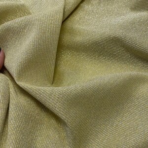 May include: Close-up of a gold metallic fabric with a ribbed texture. The fabric is soft and shimmery, with a subtle sheen.
