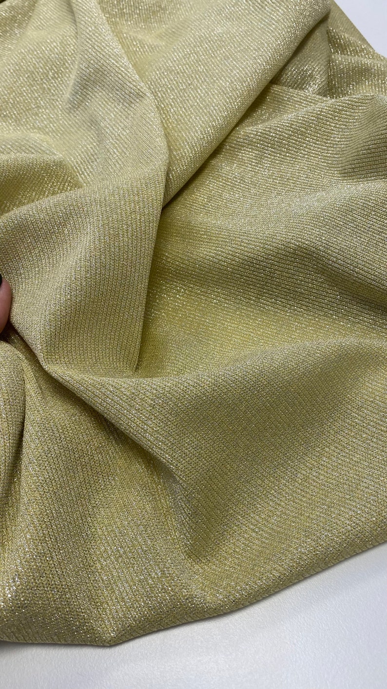 May include: Close-up of a gold metallic fabric with a ribbed texture. The fabric is soft and shimmery, with a subtle sheen.