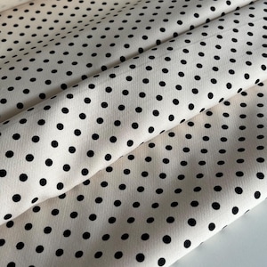 Könnte beinhalten: Cremefarbener Stoff mit schwarzem Punktmuster. Der Stoff ist in der Mitte gefaltet, sodass das Muster auf beiden Seiten sichtbar ist.