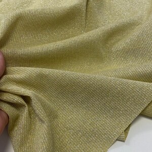 May include: A close-up of a gold metallic fabric with a ribbed texture. The fabric has a subtle sheen and is perfect for creating garments or accessories.