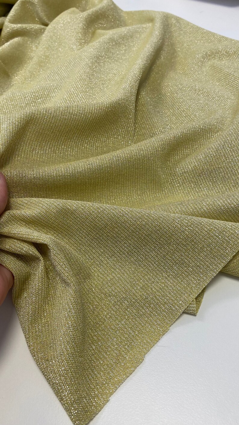 May include: A close-up of a gold metallic fabric with a ribbed texture. The fabric has a subtle sheen and is perfect for creating garments or accessories.