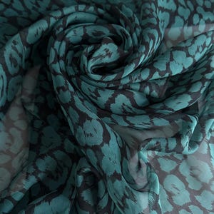 Könnte beinhalten: Gewebestoff mit einem Wirbelmuster aus teal- und schwarzen Tierdrucken. Das transparente Material ist drapiert und gefaltet, wodurch die sich wiederholenden Formen des Designs zur Geltung kommen. Die Textur und Farbvariationen erzeugen Tiefe.