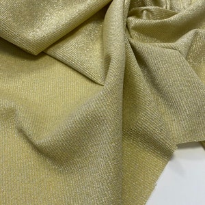 May include: A close-up of a gold fabric with a subtle shimmer. The fabric has a ribbed texture and is folded in a way that shows the texture and sheen.