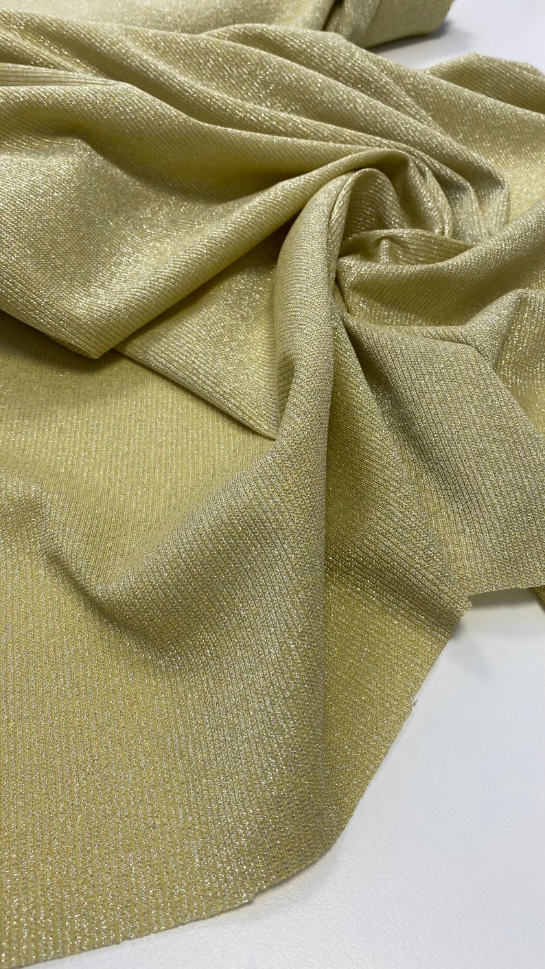 May include: A close-up of a gold fabric with a subtle shimmer. The fabric has a ribbed texture and is folded in a way that shows the texture and sheen.