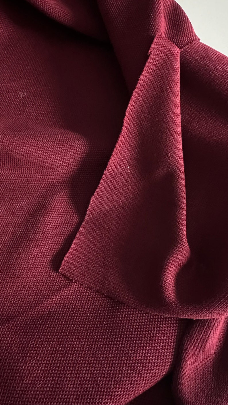 Pu&ograve; includere: Primo piano di un tessuto color borgogna con una superficie testurizzata. Il tessuto &egrave; piegato su se stesso, creando una forma triangolare.