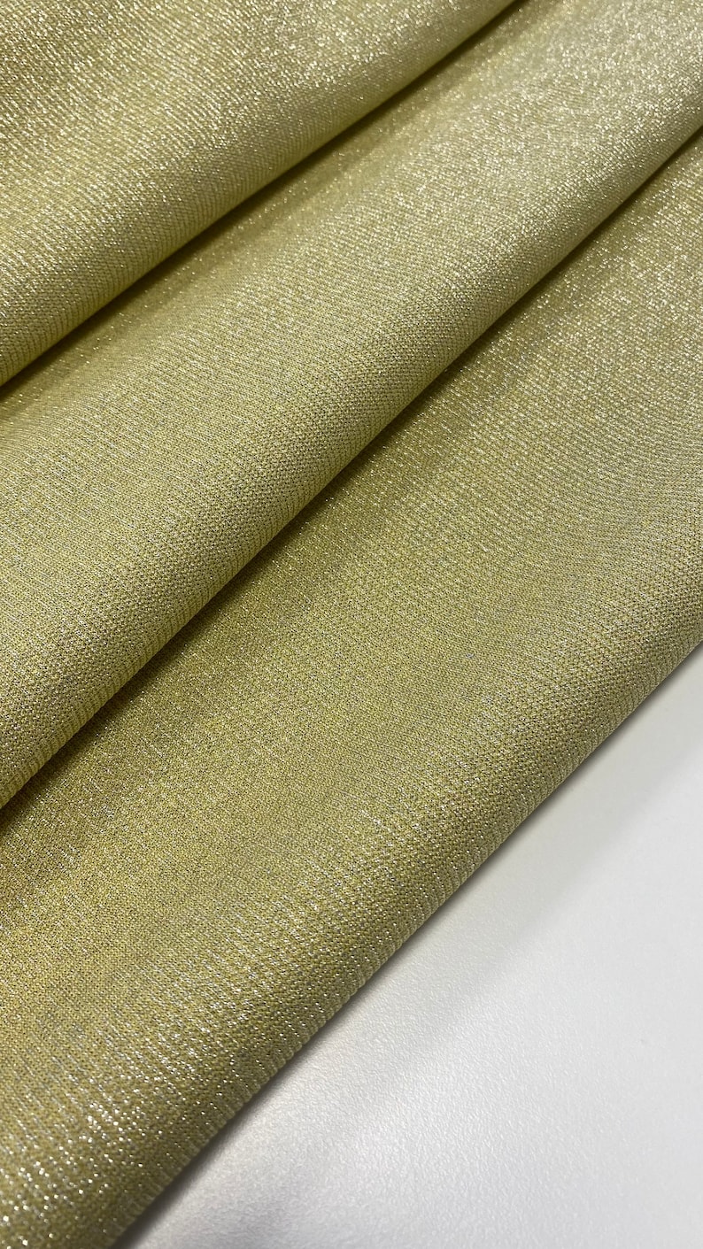 May include: A close-up of a gold fabric with a subtle shimmer. The fabric has a woven texture and a smooth, soft feel.