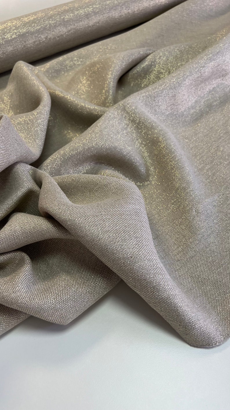 May include: A close-up of a beige fabric with a subtle shimmer. The fabric has a woven texture and a slightly metallic sheen.