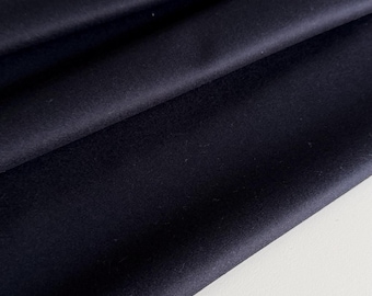 May include: Close-up of a dark navy blue fabric with soft folds. The material appears smooth and opaque, with subtle variations in tone. The fabric is likely used for clothing or home decor.
