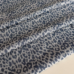 Könnte beinhalten: Nahaufnahme eines gefalteten Stoffes mit einem blau-weißen Leopardenmuster. Der Stoff ist strukturiert und scheint gewebt zu sein. Die Leopardenflecken sind in einem helleren Blauton gehalten und bilden einen Kontrast.