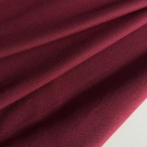 Può includere: Primo piano di un tessuto color borgogna scuro con una trama testurizzata. Il tessuto è piegato e drappeggiato, mostrando la sua texture morbida e flessibile.