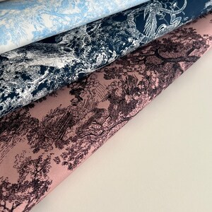 May include: Four different fabric swatches with a black and white toile pattern. The swatches are layered on top of each other, with the top swatch being a light beige color, the second swatch being a light blue color, the third swatch being a dark blue color, and the bottom swatch being a light pink color.