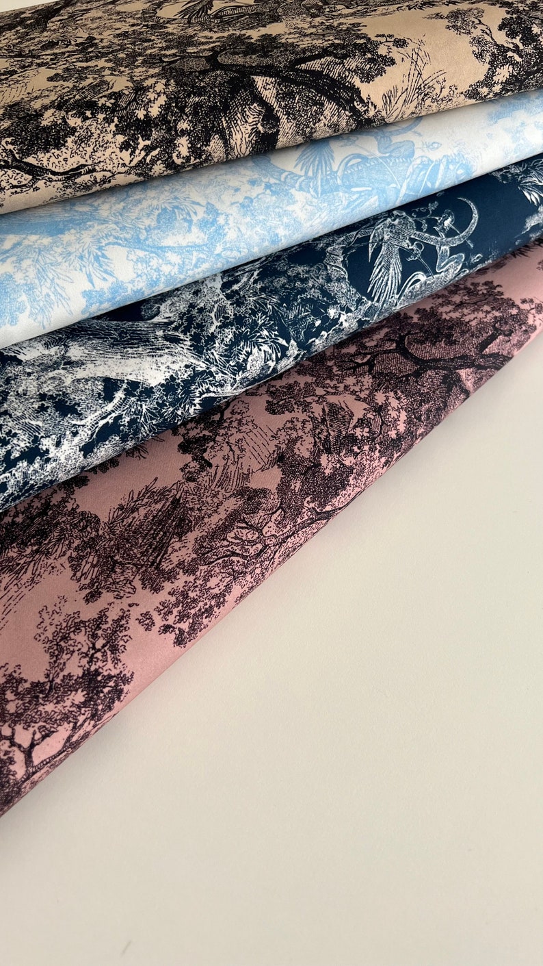 May include: Four different fabric swatches with a black and white toile pattern. The swatches are layered on top of each other, with the top swatch being a light beige color, the second swatch being a light blue color, the third swatch being a dark blue color, and the bottom swatch being a light pink color.