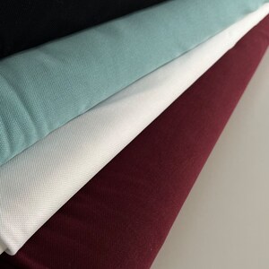 Pu&ograve; includere: Un mucchio di cinque campioni di tessuto in diversi colori. Il campione inferiore &egrave; di colore bordeaux scuro, il successivo &egrave; bianco, il successivo &egrave; di colore blu-verde chiaro, il successivo &egrave; nero e il campione superiore &egrave; di colore grigio chiaro.