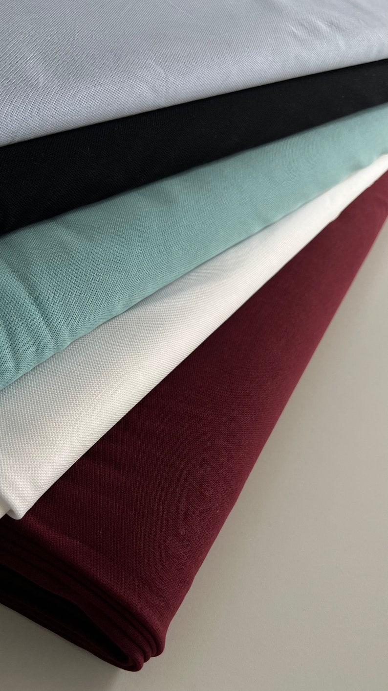 Pu&ograve; includere: Un mucchio di cinque campioni di tessuto in diversi colori. Il campione inferiore &egrave; di colore bordeaux scuro, il successivo &egrave; bianco, il successivo &egrave; di colore blu-verde chiaro, il successivo &egrave; nero e il campione superiore &egrave; di colore grigio chiaro.