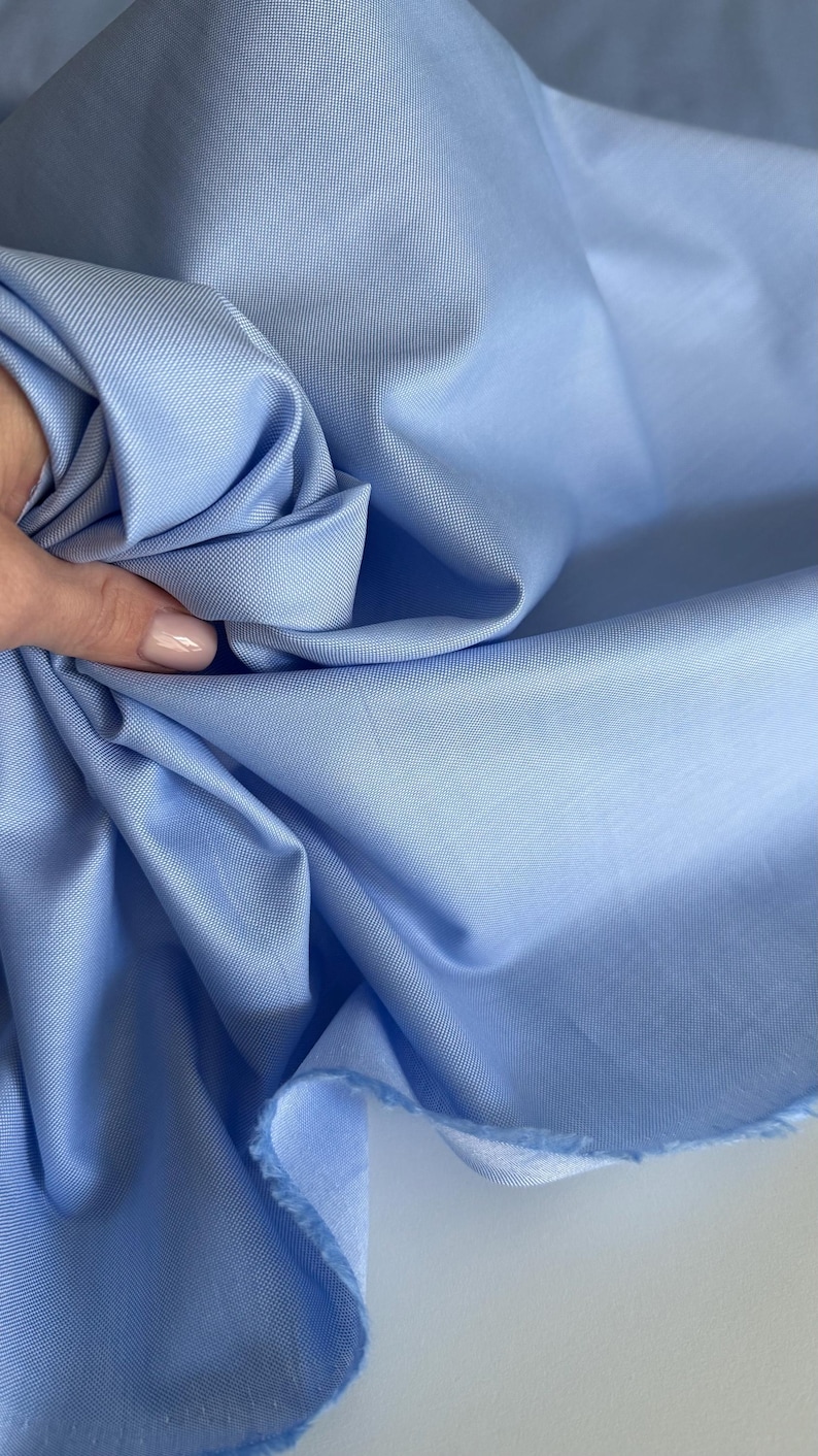 May include: A light blue fabric with a textured weave. The fabric is folded and draped, showing its soft texture.