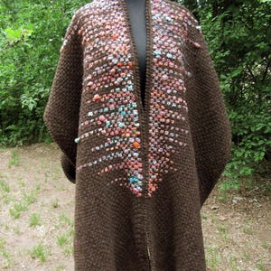 May include: A dark brown open-front cardigan featuring a textured knit pattern. The front panels are embellished with a vertical cluster of small, multi-colored raised bobbles in shades of pink, orange, blue, and white, creating a gradient effect.