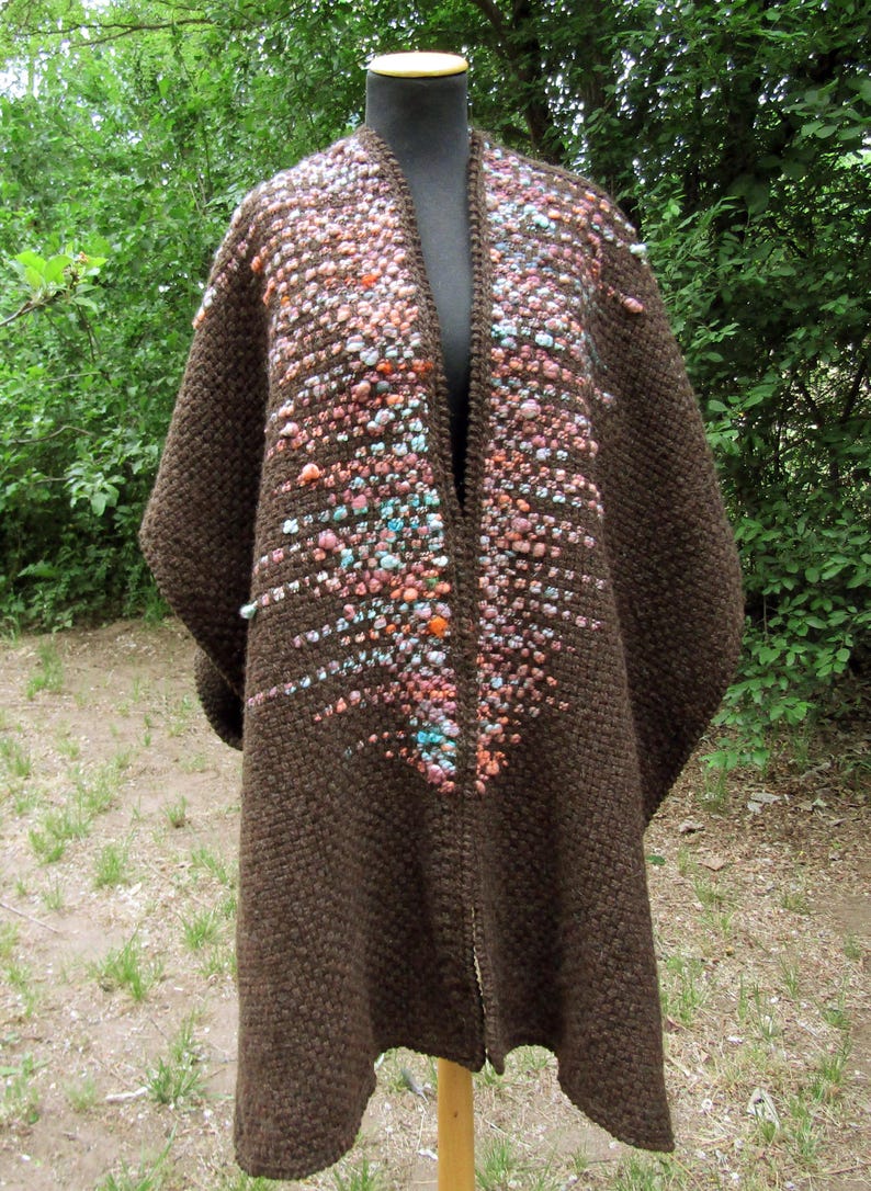 May include: A dark brown open-front cardigan featuring a textured knit pattern. The front panels are embellished with a vertical cluster of small, multi-colored raised bobbles in shades of pink, orange, blue, and white, creating a gradient effect.
