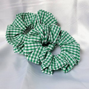 May include: Two green and white gingham scrunchies. The scrunchies are made of fabric and have a gathered look.