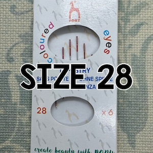 May include: A white plastic pack with a red pony logo and the text "coloured eyes". The pack contains six size 28 needles. The text "create beauty with PONY" is printed on the bottom of the pack.