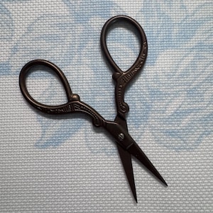 May include: Dark brown embroidery scissors with ornate handles and sharp blades. The scissors have a classic design with looped finger holes and decorative detailing. The blades are pointed and designed for precision cutting.