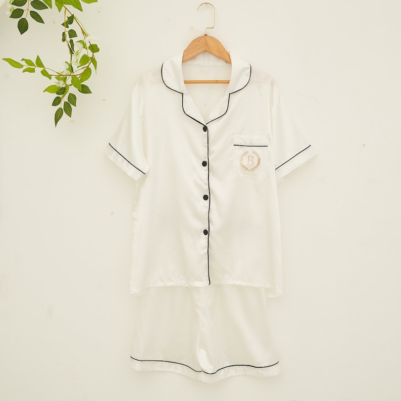 May include: White satin pajamas with black trim and a gold embroidered initial "B" on the pocket.